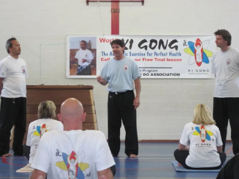 Instructors leading a World Ki Gong seminar in a gymnasium, with students standing in practice