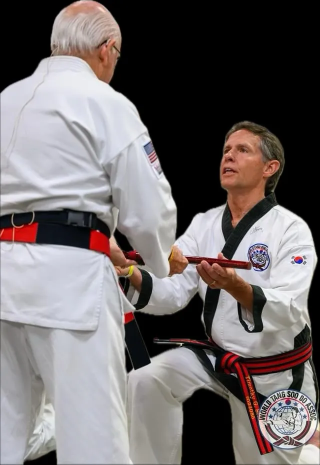 Two Tang Soo Do black belts in white dobok exchanging a certificate at a belt ceremony