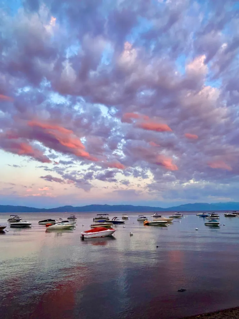 Small boats moored on a still Lake Tahoe under a pink and grey dawn sky